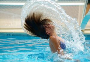 Woman surfacing from a pool dive, hair creating a circular splash.